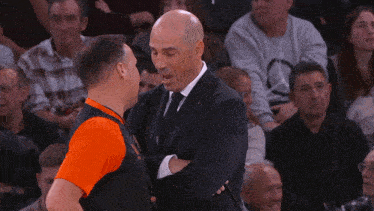 a man in a suit talks to another man in an orange shirt