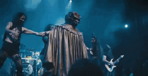 a man in a devil costume is holding a woman 's hand while playing a guitar