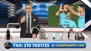 a man in a suit and tie is holding a glass of water in front of a screen that says camelot