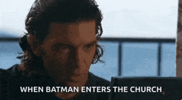 a man with long hair is looking at a computer screen with the words `` when batman enters the church '' written below him .