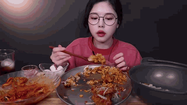 a girl with glasses is eating a plate of food with chopsticks