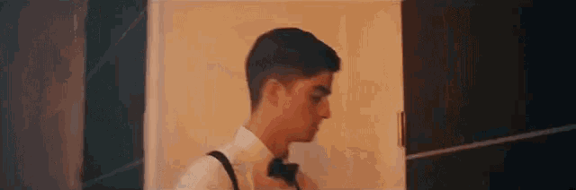 a young man in a tuxedo and bow tie is standing in a room .