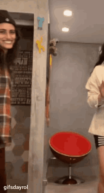 a woman in a plaid shirt is smiling while standing in front of a red chair ..