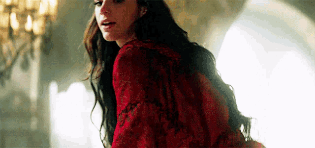 a woman in a red dress is standing in a room with a chandelier in the background .