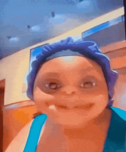 a woman wearing a purple hat and a blue tank top is making a funny face .