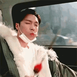 a man wearing a mask is sitting in the back seat of a car holding a red rose .