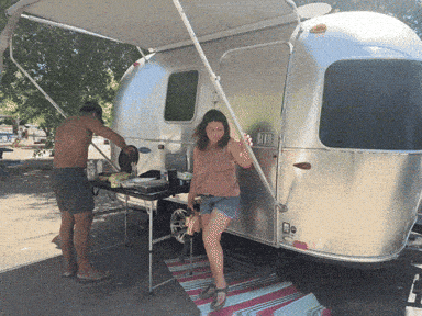 a man and a woman are standing in front of a silver airstream trailer