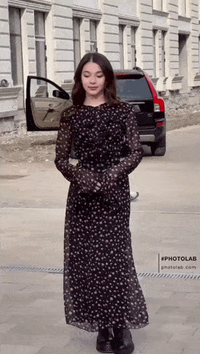 a woman in a black dress is standing in front of a black suv
