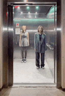 two women are standing in an elevator with a sign that says ' emergency exit ' on it