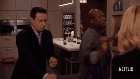 a man is opening a bottle of wine in a kitchen while a woman looks on .