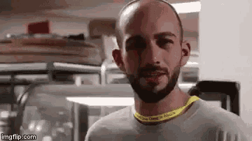 a bald man with a beard is wearing a yellow necklace and smiling .