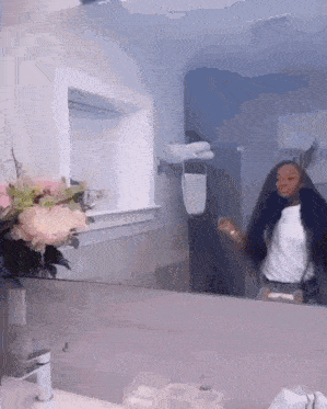 a woman is standing in front of a mirror in a bathroom with flowers on the counter .