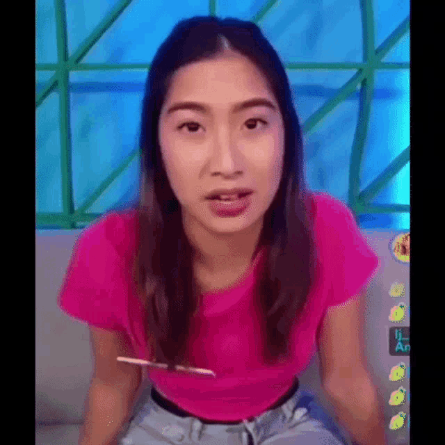 a woman in a pink shirt is sitting on a couch and holding a pencil in her mouth .