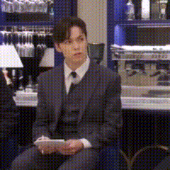 a man in a suit and tie is sitting in front of a bar holding a piece of paper .