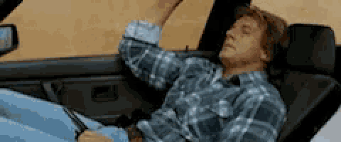 a man in a plaid shirt is sitting in a car with his arm out the window