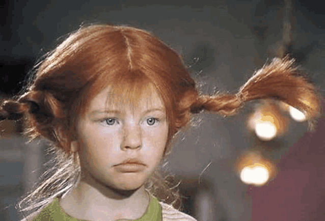 a little girl with red hair and pigtails is looking at the camera .