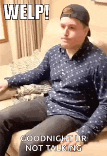 a man in a baseball cap is sitting on a couch and making a funny face .