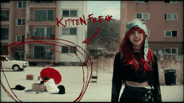 a woman with red hair is standing in front of a building with the words kitten freak written on it