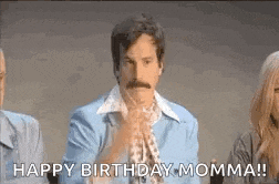 a man with a mustache is sitting in front of a group of people and saying `` happy birthday momma ! ''