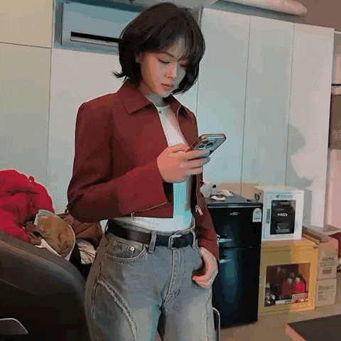 a woman in a red jacket and blue jeans is looking at her phone .