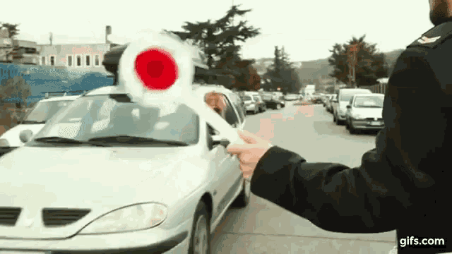 a man is holding a red and white flag in front of a silver car