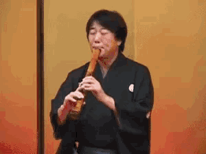 a man in a kimono is playing a flute in front of a wall .