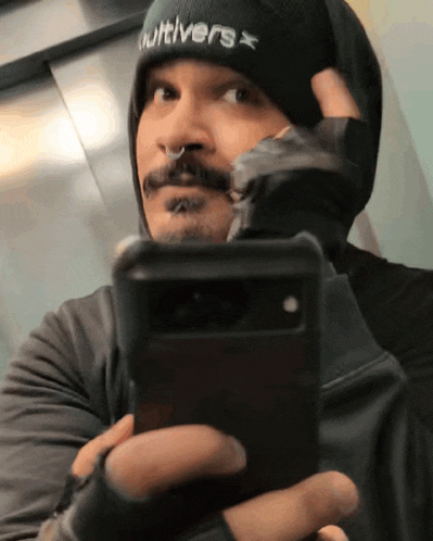 a man wearing a beanie that says cultivars takes a selfie with his phone