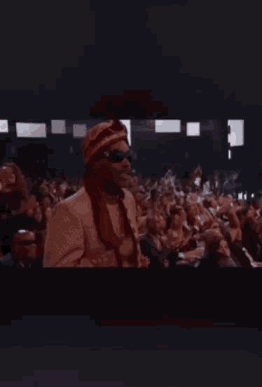 a man wearing sunglasses and a turban stands in front of a crowd of people