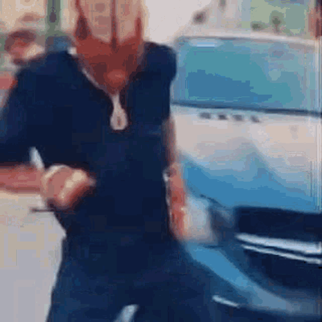 a man is standing next to a blue car and dancing .