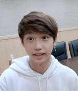a young boy wearing a white hoodie and earrings is sitting at a table .