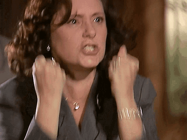 a woman in a suit is making a funny face with her fists in the air .