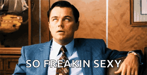 a man in a suit and tie is sitting in a chair with the words so freakin sexy written below him