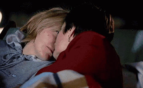 two women are laying on a blanket in a car and kissing each other .