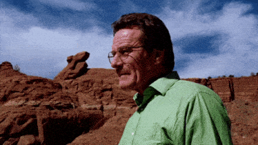 a man wearing glasses and a green shirt stands in front of rocks