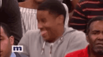 a man is sitting in a crowd of people and making a face .