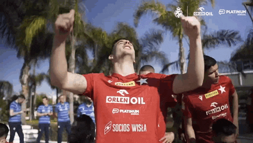 a man in a red orlen oil shirt holds his arms in the air