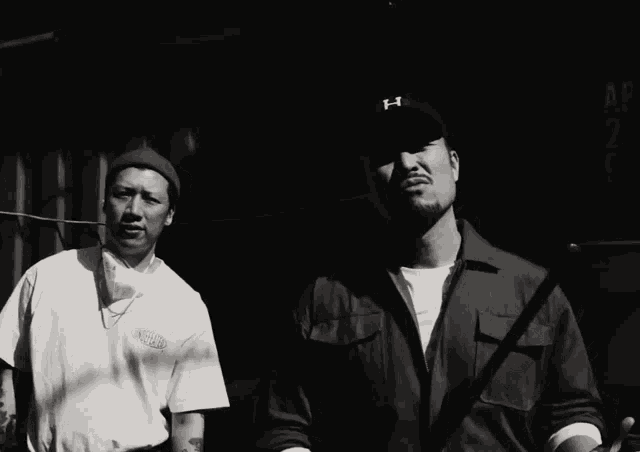 two men are standing next to each other one wearing a hat with the letter h on it