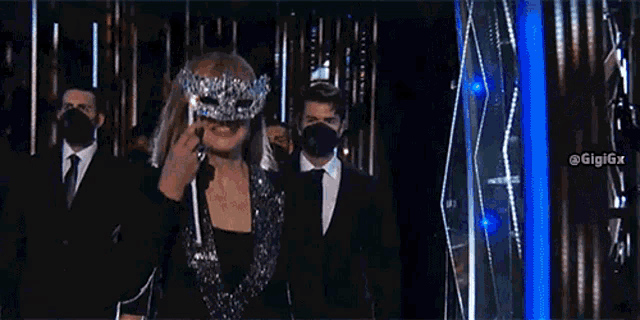 a woman is wearing a mask and smiling while standing in front of a crowd of people wearing masks .
