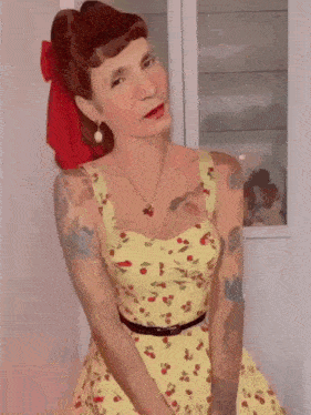 a woman in a yellow dress with cherries on it and a red bow in her hair is posing for the camera .