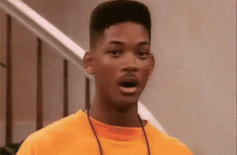 a man in an orange shirt is making a surprised face while standing in front of a staircase .