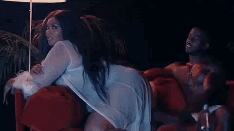 a woman is sitting on a couch next to a shirtless man in lingerie .