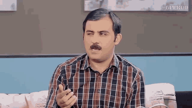 a man with a mustache is sitting on a couch and talking