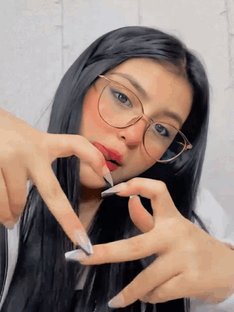 a woman with long black hair and glasses is making a heart shape with her hands