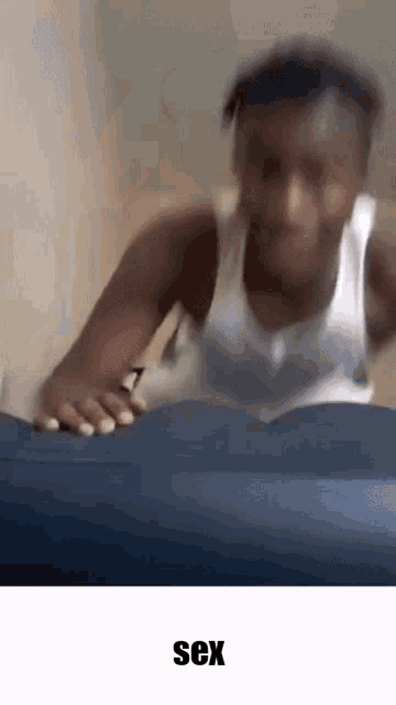 a man in a white tank top is laying on a blue blanket with the word sex in the corner .