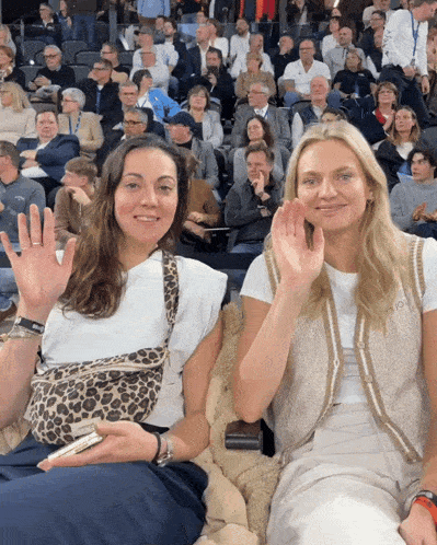 two women waving their hands in front of a crowd at a sporting event