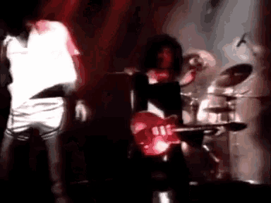 a man is playing a red guitar on a stage while a woman is dancing behind him .