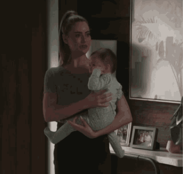 a woman is holding a baby in her arms in front of a wall with pictures on it
