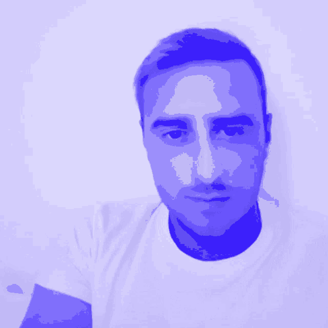 a man wearing a white shirt with a blue background looks at the camera