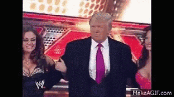 a man in a suit and tie is standing next to two women in wrestling costumes .