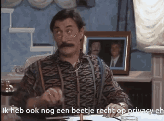 a man with glasses and a mustache is sitting at a table and says ik heb ook nog een beetje recht op privacy en